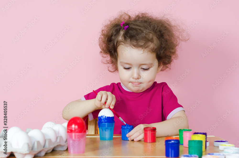 Smiling cute girl with brush paints white eggs in trend colors. baby is preparing for Easter. Smiling cute girl with brush paints white eggs in trend colors. baby is preparing for Easter.