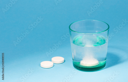 Dissolving an effervescent tablet in a glass of water at blue background with copy space