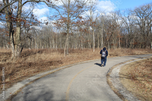 Man walking with a backpack on the North Branch Trail in early spring at Miami Woods in Morton Grove, Illinois
