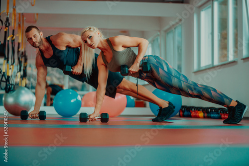 Beautiful young sports people are working out with dumbbells in gym