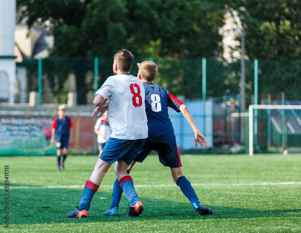 Boys in white and blue sportswear plays football on field, dribbles ball. Young soccer players with ball on green grass. Training, football, active lifestyle for kids concept Boys in white and blue sportswear plays football on field, dribbles ball. Young soccer players with ball on green grass. Training, football, active lifestyle for kids concept