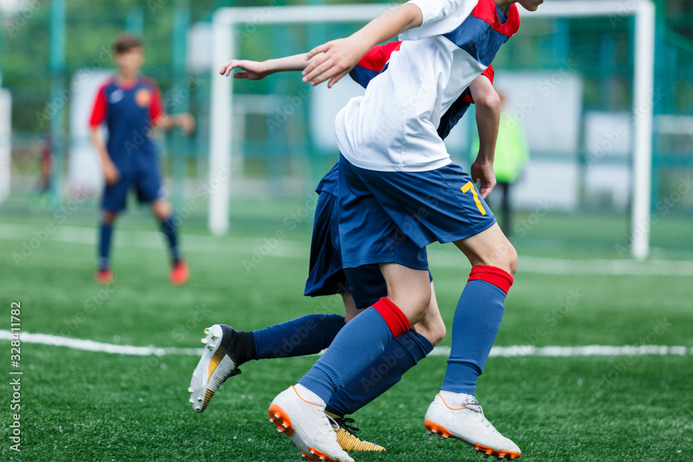Boys in white and blue sportswear plays football on field, dribbles ball. Young soccer players with ball on green grass. Training, football, active lifestyle for kids concept Boys in white and blue sportswear plays football on field, dribbles ball. Young soccer players with ball on green grass. Training, football, active lifestyle for kids concept