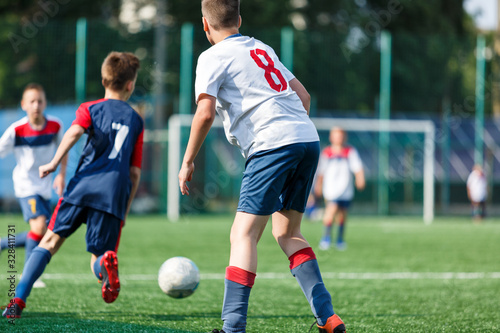 Boys in white and blue sportswear plays football on field, dribbles ball. Young soccer players with ball on green grass. Training, football, active lifestyle for kids concept