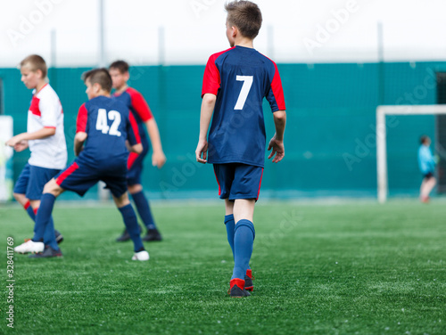 Boys in white and blue sportswear plays football on field, dribbles ball. Young soccer players with ball on green grass. Training, football, active lifestyle for kids concept