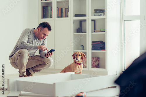 Man using a mobile phone while making furniture with his dog. © kerkezz