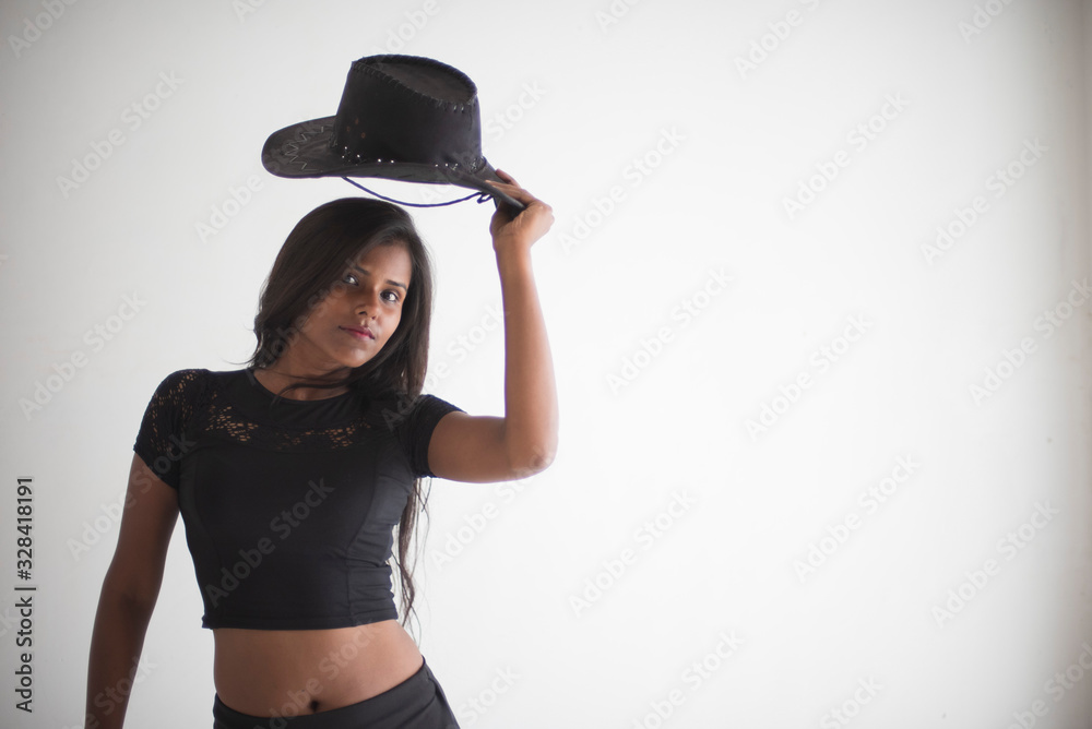 Portrait of an attractive young brunette dark skinned Indian Bengali girl in black western sportswear with a hat standing in white studio background. Indian lifestyle Portrait of an attractive young brunette dark skinned Indian Bengali girl in black western sportswear with a hat standing in white studio background. Indian lifestyle