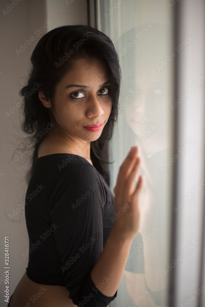 Portrait of an attractive young brunette Indian Bengali girl in western sportswear in front a glass window in white studio background. Indian lifestyle Portrait of an attractive young brunette Indian Bengali girl in western sportswear in front a glass window in white studio background. Indian lifestyle