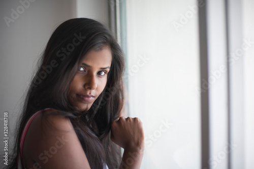 Portrait of an attractive young brunette dark skinned Indian Bengali girl in western sportswear in front a glass window in white studio background. Indian lifestyle