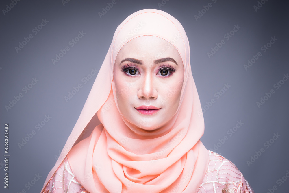 Headshot of a beautiful Muslim female model in an Asian Muslim traditional dress and hijab isolated on grey background. Eidul fitri fashion and lifestyle portrait concept Headshot of a beautiful Muslim female model in an Asian Muslim traditional dress and hijab isolated on grey background. Eidul fitri fashion and lifestyle portrait concept