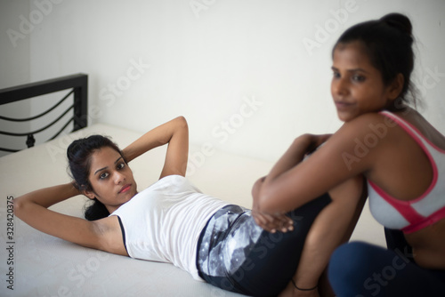 Indian black and white brunette girls are helping each other while performing yoga/sports /exercise in sportswear in front of a white background. Indian lifestyle