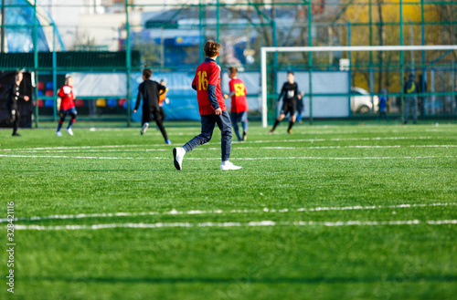 Boys in red and black sportswear plays football on field, dribbles ball. Young soccer players with ball on green grass. Training, football, active lifestyle for kids concept © Natali