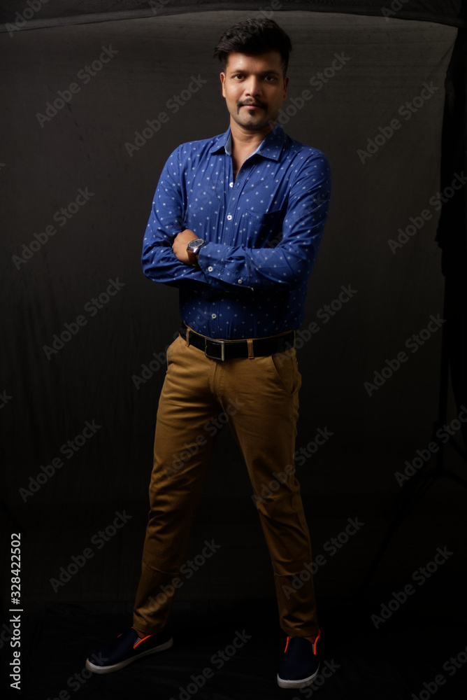 Portrait of a handsome and intelligent Indian brunette man wearing blue shirt with white stars standing before a copy space black background. Indian lifestyle and fashion portrait Portrait of a handsome and intelligent Indian brunette man wearing blue shirt with white stars standing before a copy space black background. Indian lifestyle and fashion portrait