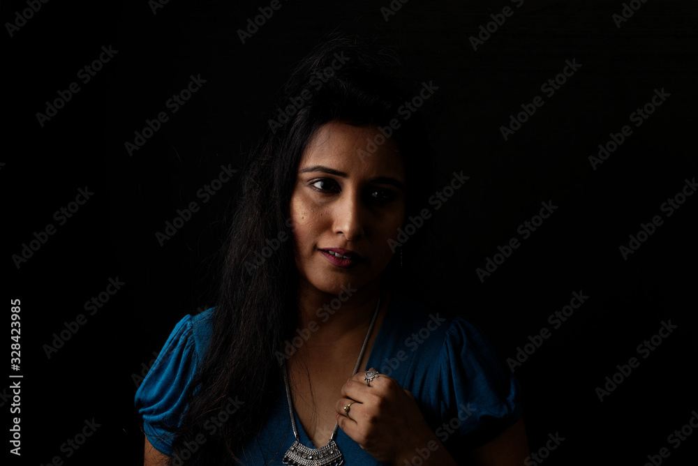Close up face portrait of a beautiful Indian Bengali brunette woman in light and shadow before a black copy space background wearing a blue top. Indian lifestyle and fashion  portrait