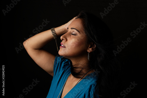 Close up face portrait of a beautiful Indian Bengali brunette woman in light and shadow before a black copy space background wearing a blue top. Indian lifestyle and fashion  portrait