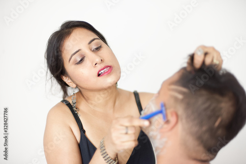 Attractive Indian Bengali brunette couple seductive foreplay in black dress in a white bedroom while the girl is shaving the man in a seductive way.  Indian lifestyle 