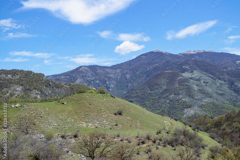 Mountains landscape, sunny day. White clouds on a blue sky. The mountains are covered with green vegetation.