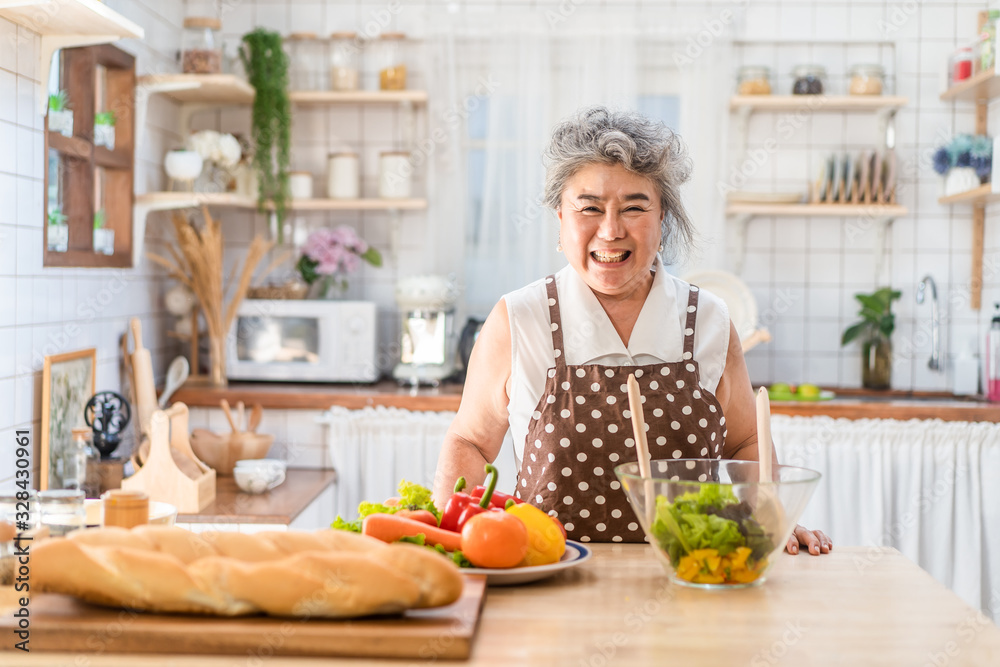Senior Asian elder woman happy living in home kitchen. Grandmother cooking salad dish standing at counter with happiness and smile enjoy retirement life. Older people activity in family at home.
