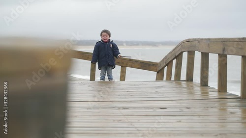 Slow motion of sad, angry child crying at woodem pathway at seashore. Background of sea and sandunes landscape. Jose Ignacio, Rocha, Uruguay photo