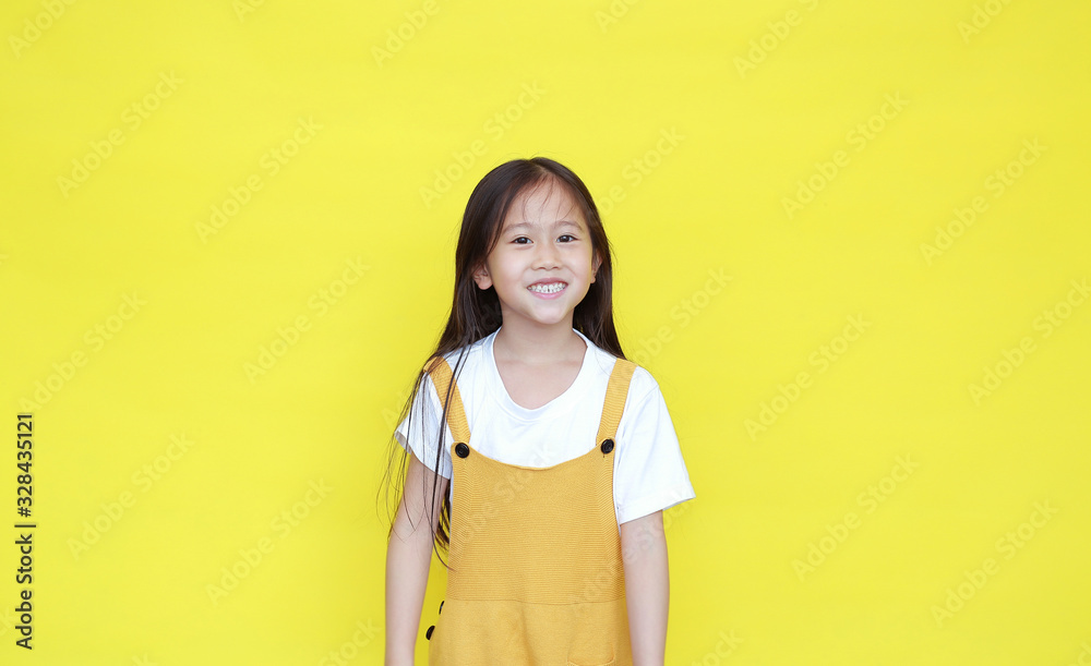 Portrait of happy asian little girl in dungarees with smiling isolated on yellow background Portrait of happy asian little girl in dungarees with smiling isolated on yellow background