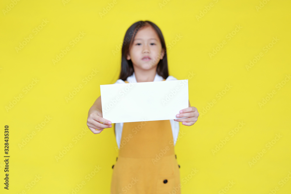 Asian little child girl holding blank sheet of paper for advertising on yellow background. Kid holding empty banner for information concept. Focus at paper in his hands. Asian little child girl holding blank sheet of paper for advertising on yellow background. Kid holding empty banner for information concept. Focus at paper in his hands.