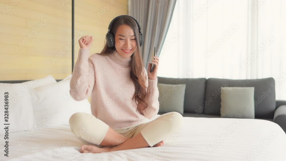 Pretty Asian girl grooving to dance music through bluetooth headphones while in bedroom. Fixed shot, Full shot. Pretty Asian girl grooving to dance music through bluetooth headphones while in bedroom. Fixed shot, Full shot.