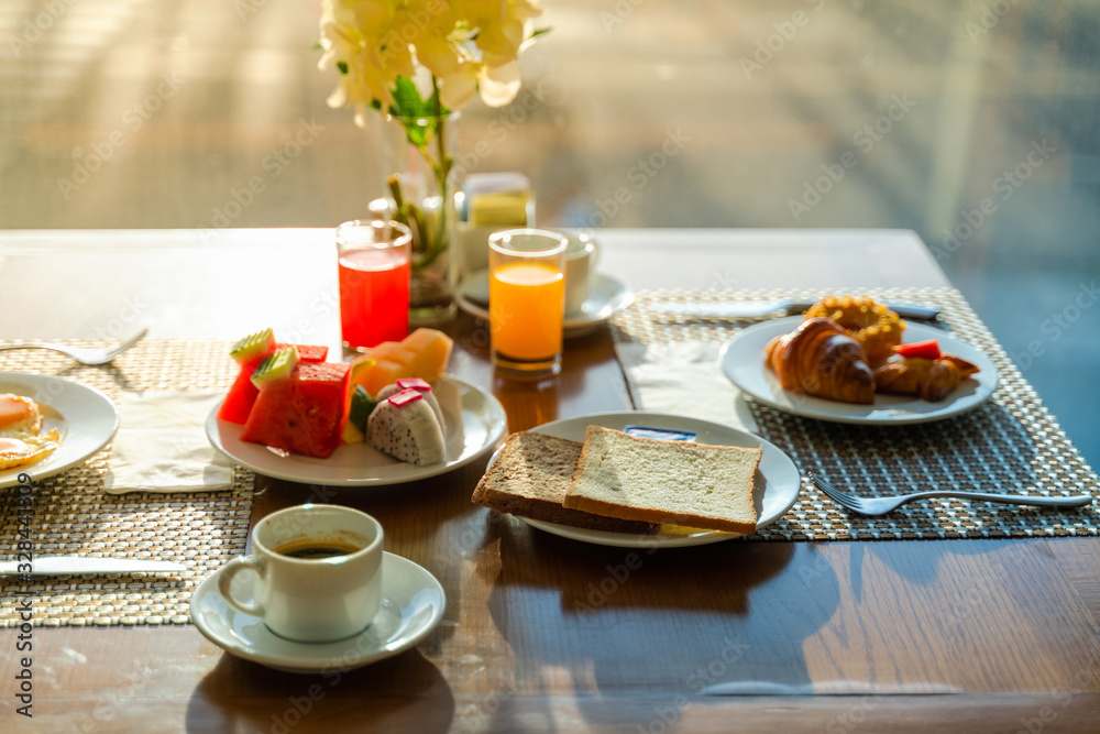 Fresh romantic breakfast table next to morning briliant light window, with coffee cup, bread, fruit, juice, egg...