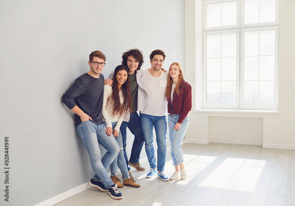 A group of smiling friends is standing in a bright room with a window.