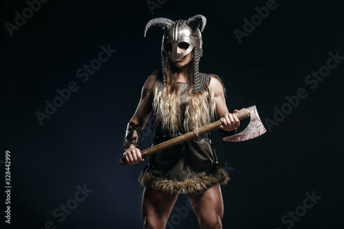 Beautiful female viking woman warrior in battle with big two-handed axe and helmet with horns. Ancient times. Amazon fantasy blonde hair sexy girl.