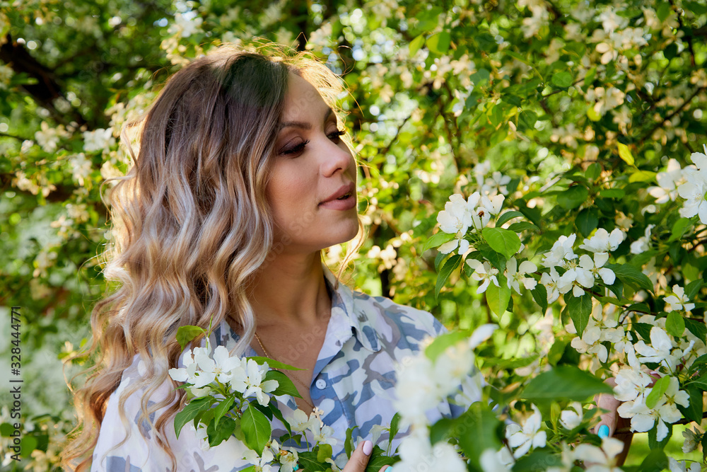 Portrait of a beautiful blonde girl with green eyes and blossoming apple tree with white flower in the park in a spring time Portrait of a beautiful blonde girl with green eyes and blossoming apple tree with white flower in the park in a spring time