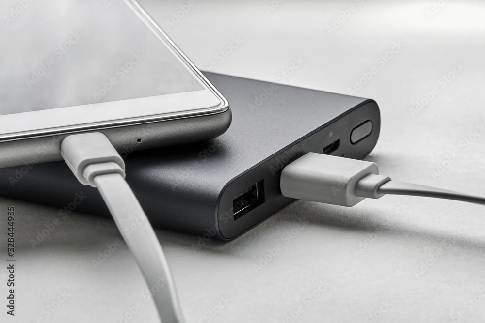 The smartphone is charging from external powerbank with cable. White background, closeup, selective focus The smartphone is charging from external powerbank with cable. White background, closeup, selective focus