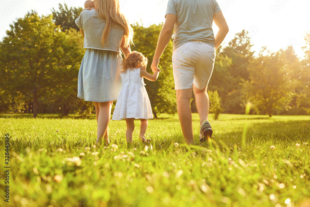 Fototapeta premium Happy family walking on the grass in the summer park. Mother father and children playing in nature.