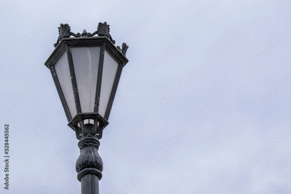 Vintage street lamp. Black paint with exfoliation. Background sky.