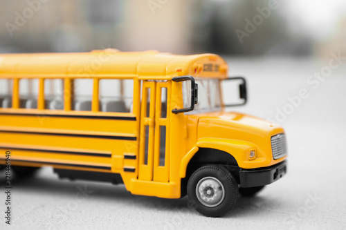 Yellow toy school bus against blurred background, closeup. Transport for students