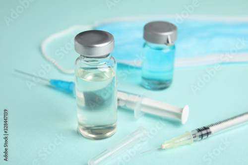 Vials, syringes and surgical mask on turquoise background. Vaccination and immunization