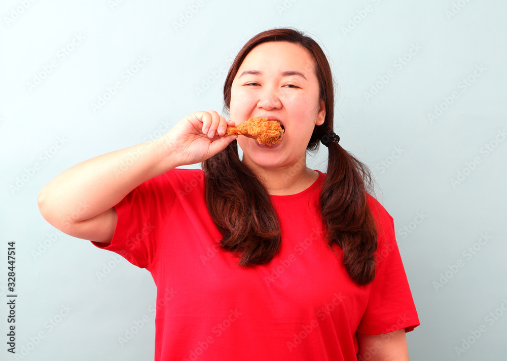Funny face Asian woman is eating fried chicken deliciously,isolated on blue background in studio With copy space. Funny face Asian woman is eating fried chicken deliciously,isolated on blue background in studio With copy space.