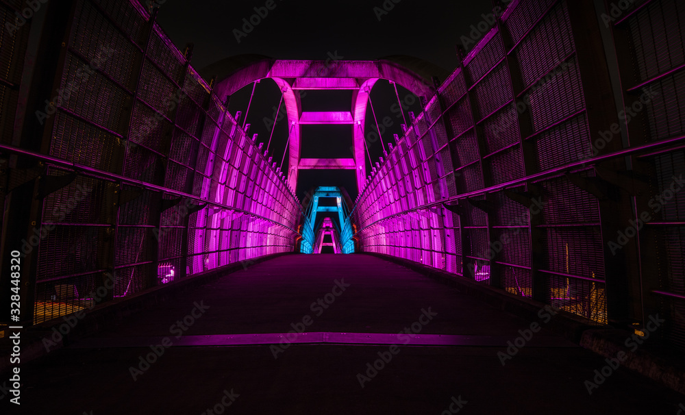 Bright purple leds illuminate pedestrian walkway over highway at night