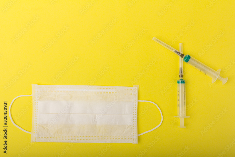 White medical mask and medical syringe isolated on yellow background. Face mask protection against pollution, virus, flu and coronavirus. White medical mask and medical syringe isolated on yellow background. Face mask protection against pollution, virus, flu and coronavirus.