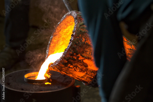 Molten bronze poured into mold by melter in foundry workshop