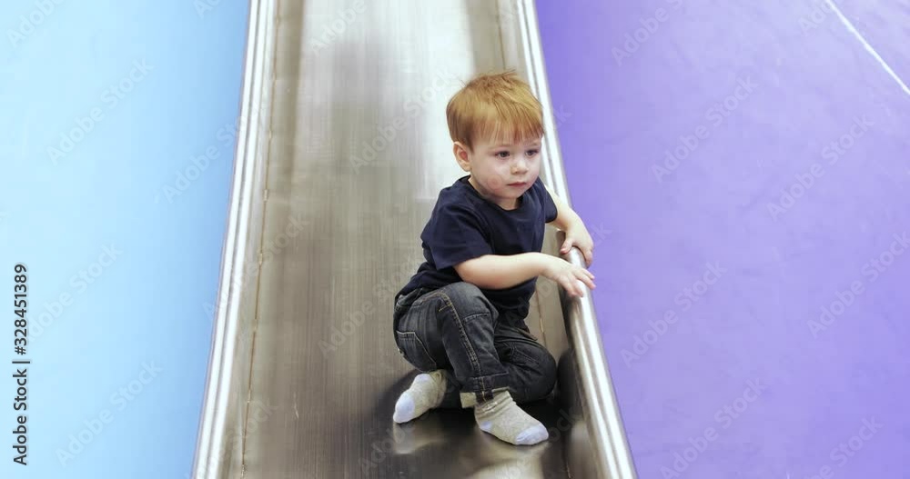 Infant boy plays on a metalic slide