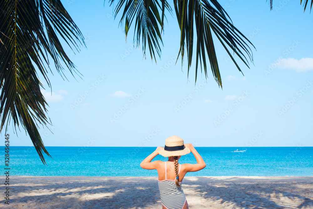 Kid in swimsuit and straw hat standing on the sea beach with palm tree Kid in swimsuit and straw hat standing on the sea beach with palm tree