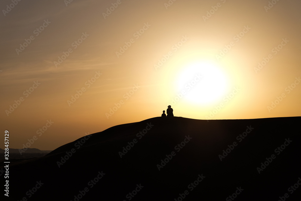 A boy and a man in Arabic national costumes look at the landscape in the RUB al-Khali desert . Silhouettes against a sunset in the desert