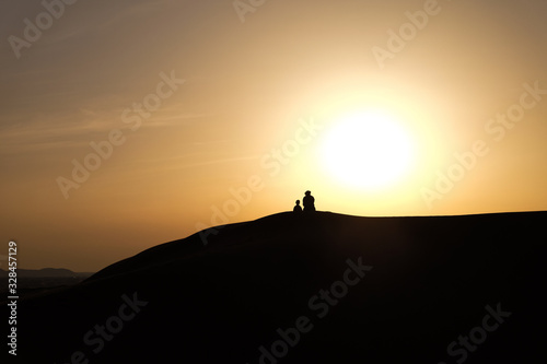 A boy and a man in Arabic national costumes look at the landscape in the RUB al-Khali desert . Silhouettes against a sunset in the desert © Евгений Симдянкин