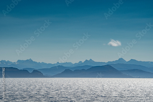 Land in Sicht - Verblauung der K  ste in Norwegen mit Meer  Bergen  blauem Himmel und einzelner Wolke von der Seeseite aus gesehen