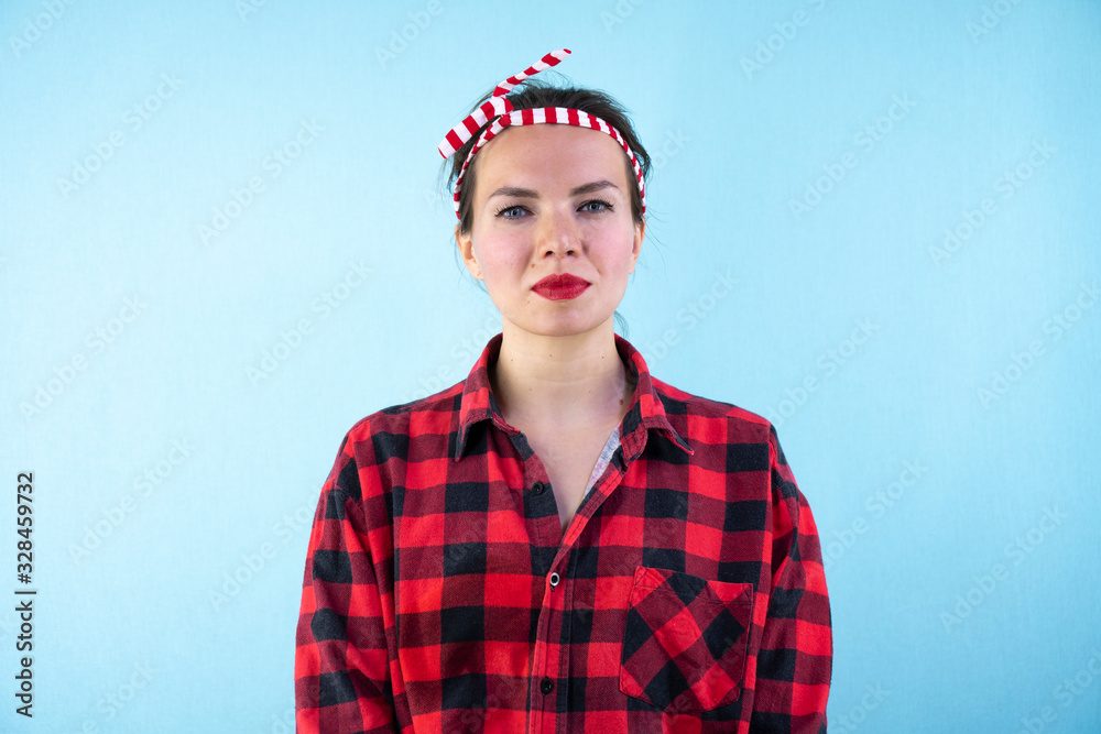 Fototapeta premium Lovely woman retro portrait with pin-up make-up and hairstyle. Red shirt. Blue background