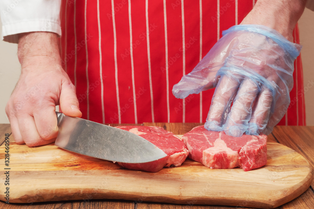 Butcher with knife in his hand and other hand on freshly cut juicy ribeye steaks.