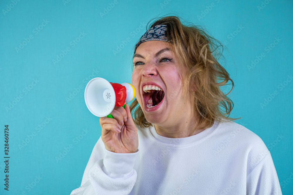 Curly stylish woman shouting into a megaphone and gesturing on a blue background Curly stylish woman shouting into a megaphone and gesturing on a blue background