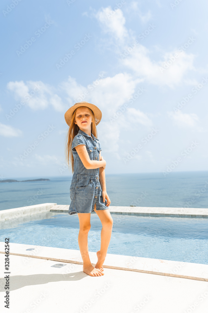 Little girl with red hair shows different emotions. Sadness, joy and happiness. She smiles and cries. In jeans with skin pigment on his face, freckles overlooking the sea. FASHIONABLE CHILD