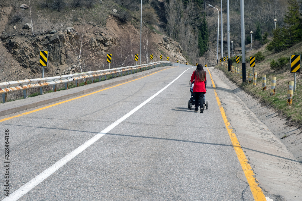 Woman is pushing baby stroller on dangerous road in mountains.