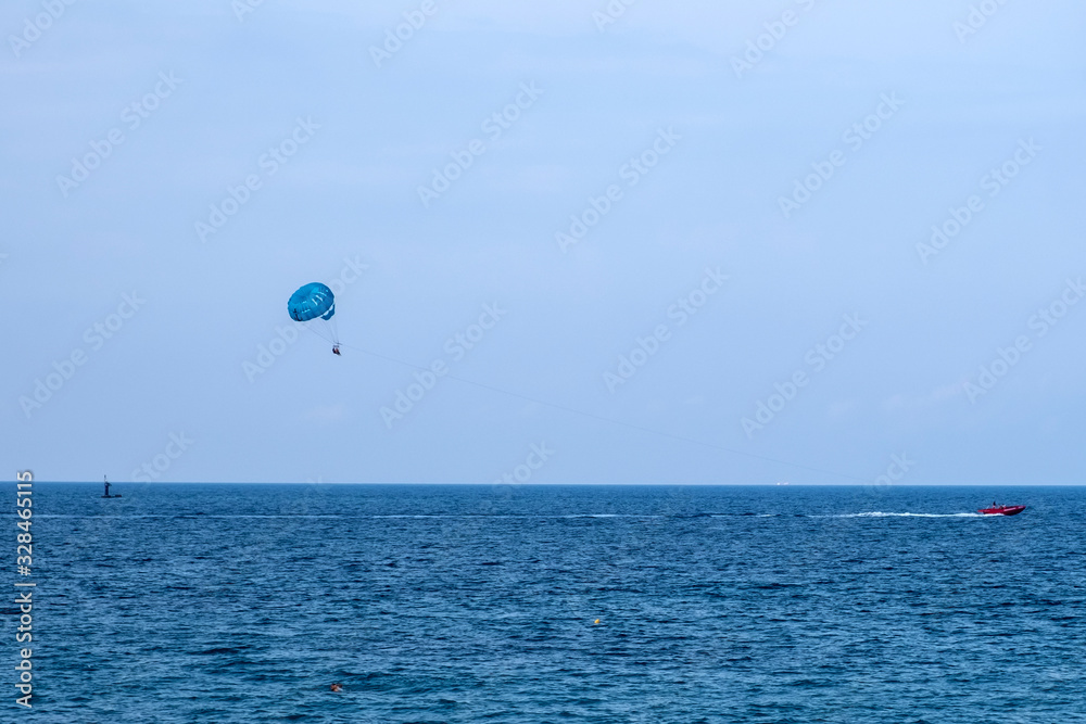 Parasailing water amusement - flying on a parachute behind a boat on a summer holiday. Tourist with parasailing on ocean sea with blue sky background. Parasailing water amusement - flying on a parachute behind a boat on a summer holiday. Tourist with parasailing on ocean sea with blue sky background.