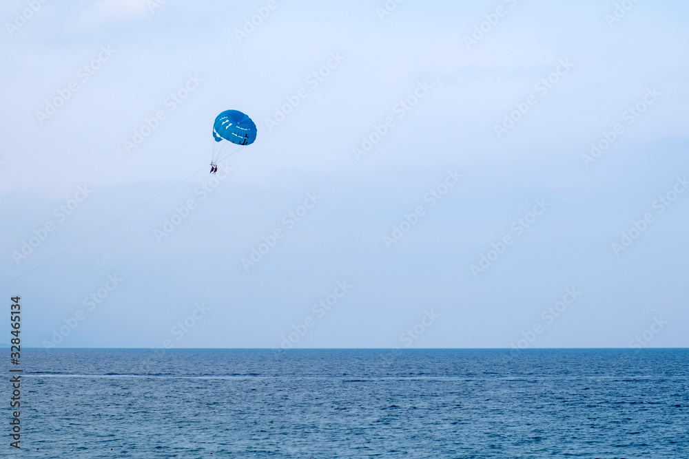 Parasailing water amusement - flying on a parachute behind a boat on a summer holiday. Tourist with parasailing on ocean sea with blue sky background. Parasailing water amusement - flying on a parachute behind a boat on a summer holiday. Tourist with parasailing on ocean sea with blue sky background.